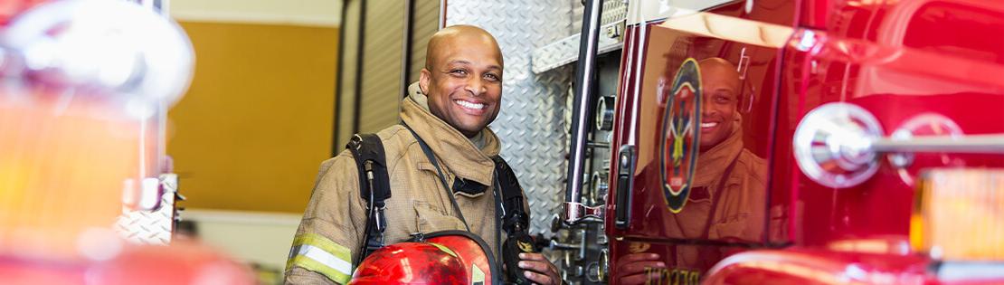 A firefighter poses smiling in gear on a fire engine